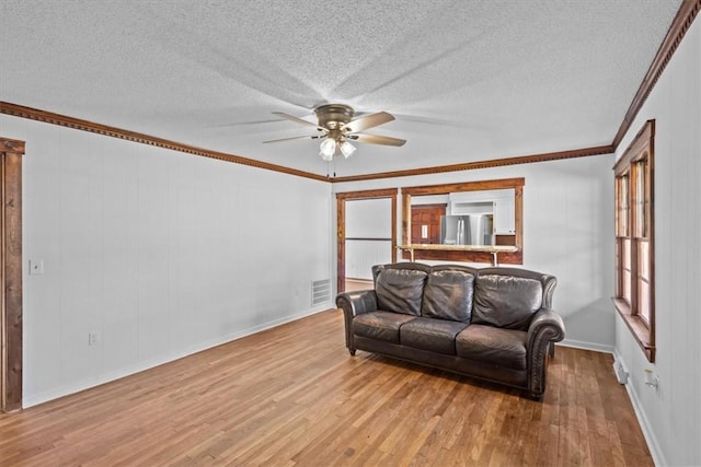 living room with ceiling fan, light wood-type flooring, a textured ceiling, and ornamental molding