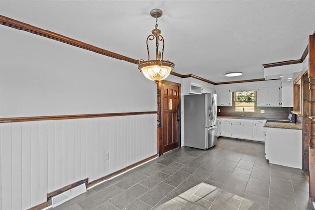 kitchen with stainless steel fridge, ornamental molding, sink, pendant lighting, and white cabinetry