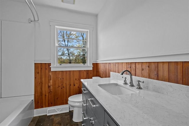 bathroom featuring wooden walls, hardwood / wood-style floors, vanity, and toilet