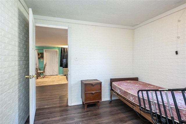 bedroom featuring a textured ceiling, dark hardwood / wood-style floors, and brick wall