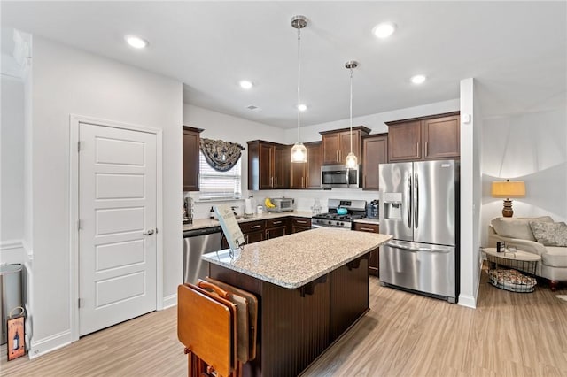 kitchen featuring appliances with stainless steel finishes, decorative light fixtures, a kitchen island, and light hardwood / wood-style flooring