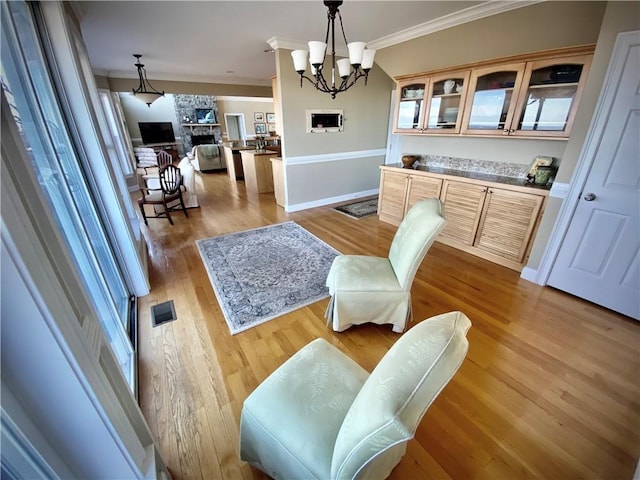 dining area featuring a stone fireplace, crown molding, a notable chandelier, and light wood-type flooring