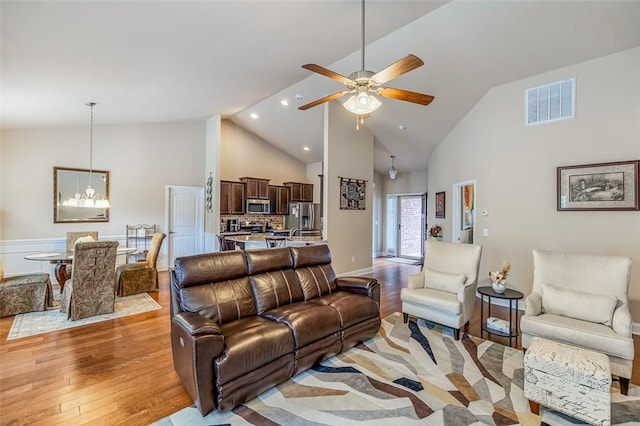 living room with ceiling fan with notable chandelier, high vaulted ceiling, and light hardwood / wood-style flooring