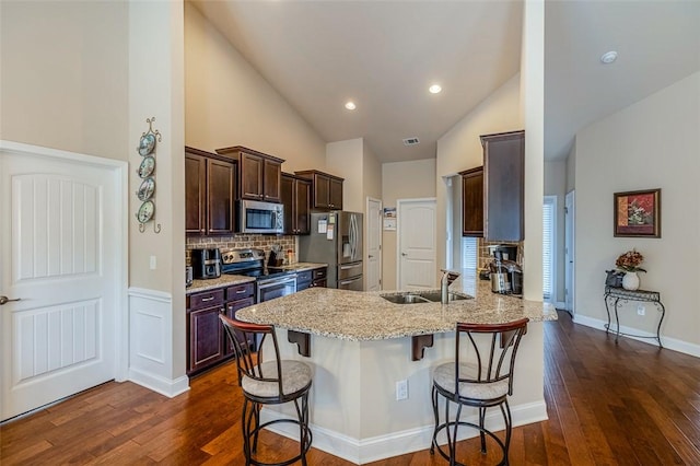 kitchen featuring kitchen peninsula, light stone countertops, appliances with stainless steel finishes, a kitchen breakfast bar, and sink