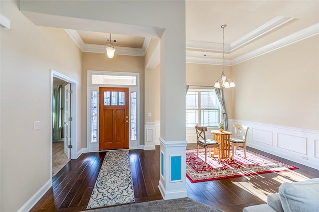 entryway with ornamental molding, dark wood-type flooring, a tray ceiling, and an inviting chandelier