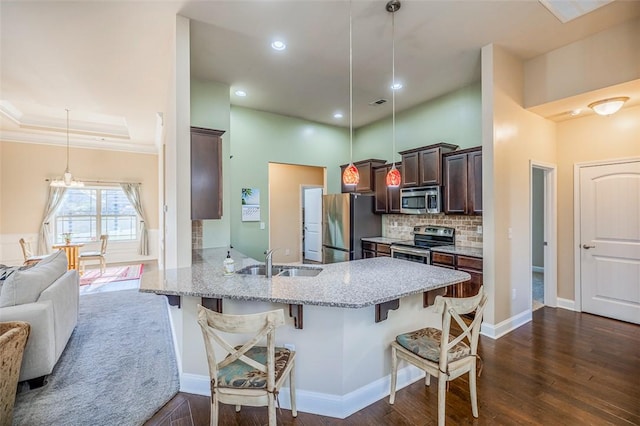 kitchen featuring dark wood-type flooring, a kitchen breakfast bar, sink, appliances with stainless steel finishes, and decorative light fixtures