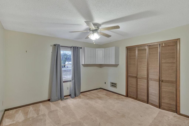 unfurnished bedroom with light carpet, a textured ceiling, a closet, and ceiling fan