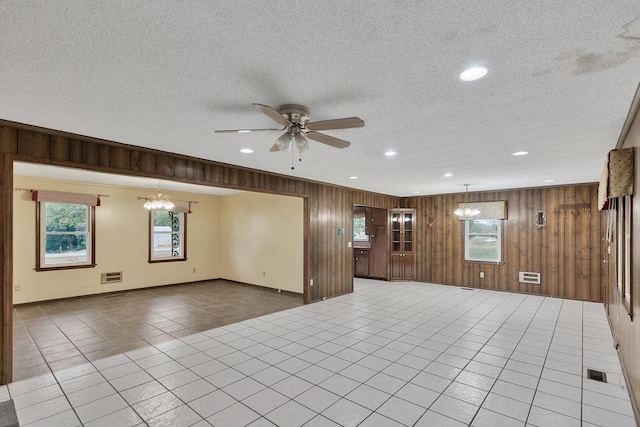 tiled spare room with a textured ceiling, ceiling fan with notable chandelier, and wood walls