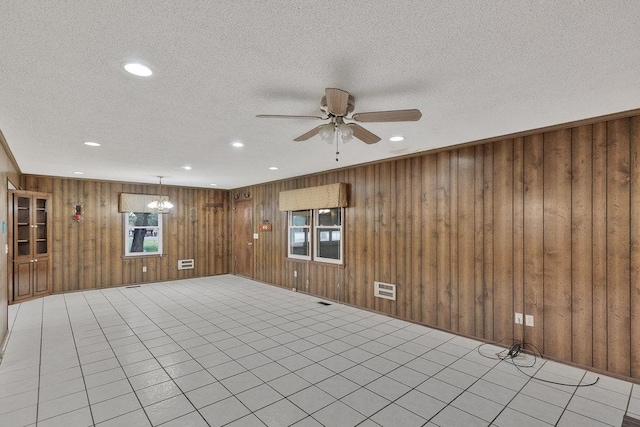 interior space with ceiling fan with notable chandelier, light tile patterned flooring, a textured ceiling, and wooden walls