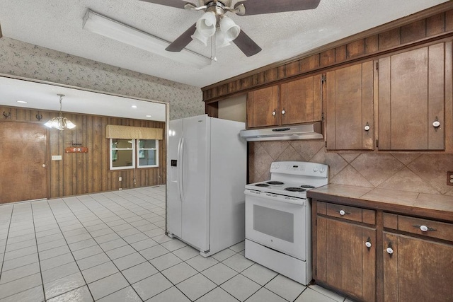 kitchen featuring white appliances, ceiling fan with notable chandelier, hanging light fixtures, wooden walls, and light tile patterned floors