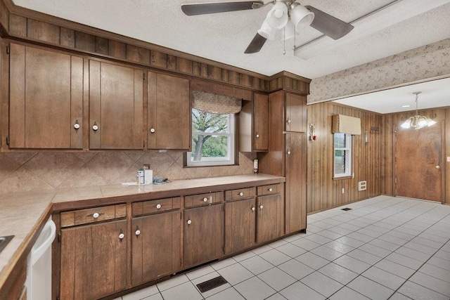 kitchen with hanging light fixtures, wood walls, a textured ceiling, light tile patterned flooring, and ceiling fan with notable chandelier