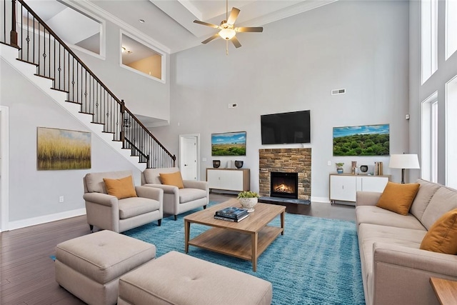 living room with a towering ceiling, dark hardwood / wood-style floors, a stone fireplace, and ceiling fan