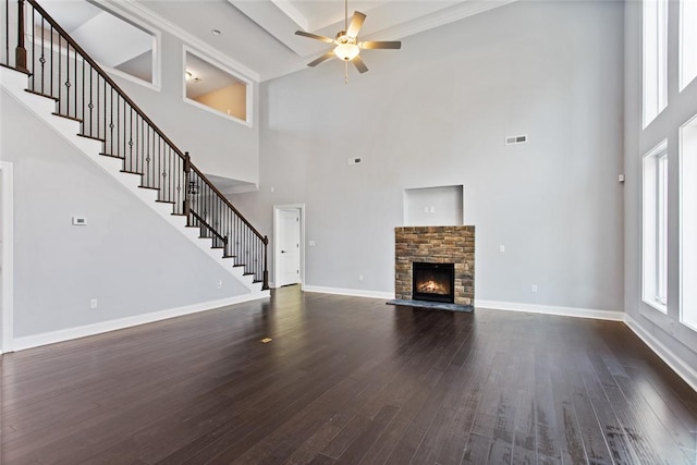 unfurnished living room with a high ceiling, dark hardwood / wood-style flooring, a stone fireplace, and ceiling fan