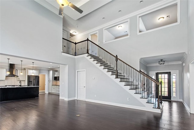 unfurnished living room with ceiling fan, dark hardwood / wood-style flooring, a towering ceiling, and crown molding