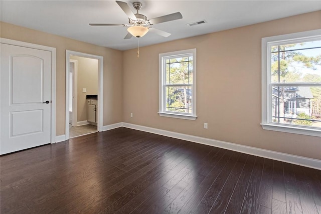 unfurnished bedroom with connected bathroom, multiple windows, ceiling fan, and dark hardwood / wood-style flooring