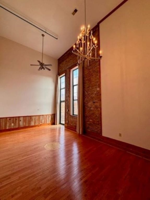 spare room with lofted ceiling, hardwood / wood-style floors, brick wall, and ceiling fan with notable chandelier