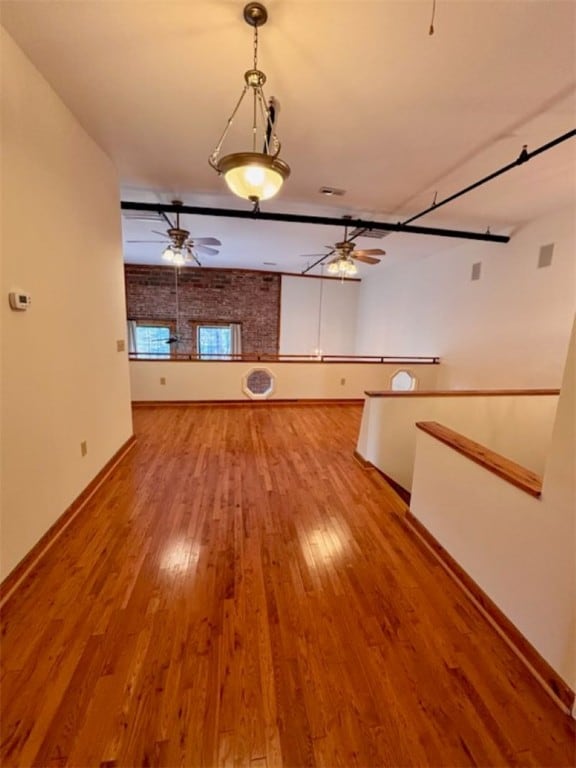 unfurnished living room with ceiling fan, brick wall, and light wood-type flooring