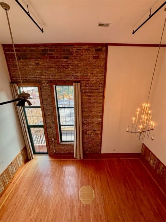 spare room featuring a chandelier, hardwood / wood-style floors, and brick wall