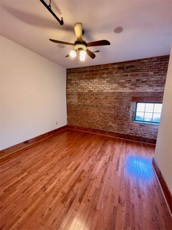 spare room featuring hardwood / wood-style flooring, ceiling fan, and brick wall