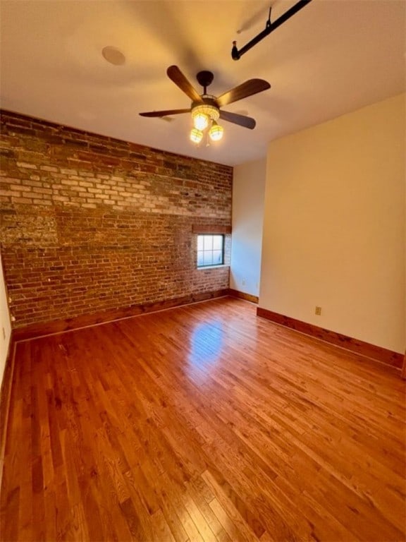 unfurnished room featuring hardwood / wood-style floors, ceiling fan, and brick wall