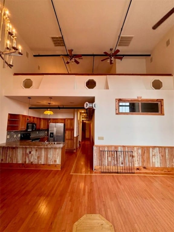 kitchen featuring kitchen peninsula, decorative backsplash, a high ceiling, stainless steel fridge with ice dispenser, and light hardwood / wood-style floors