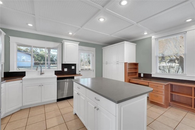 kitchen featuring stainless steel dishwasher, sink, white cabinets, a kitchen island, and light tile patterned flooring