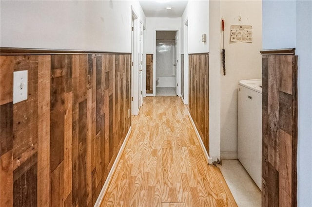 corridor with wood walls, washer / dryer, and light hardwood / wood-style flooring