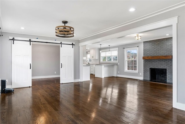 unfurnished living room featuring a barn door, crown molding, dark hardwood / wood-style flooring, and a fireplace