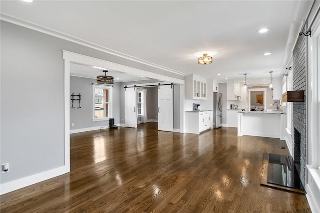 unfurnished living room featuring dark wood-type flooring, sink, crown molding, a barn door, and a fireplace