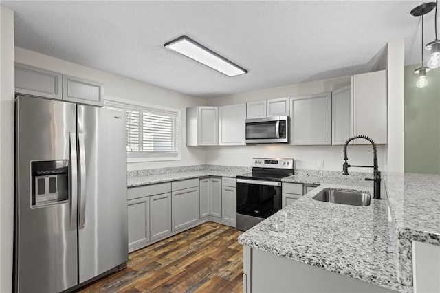 kitchen with sink, dark wood-type flooring, hanging light fixtures, light stone counters, and appliances with stainless steel finishes