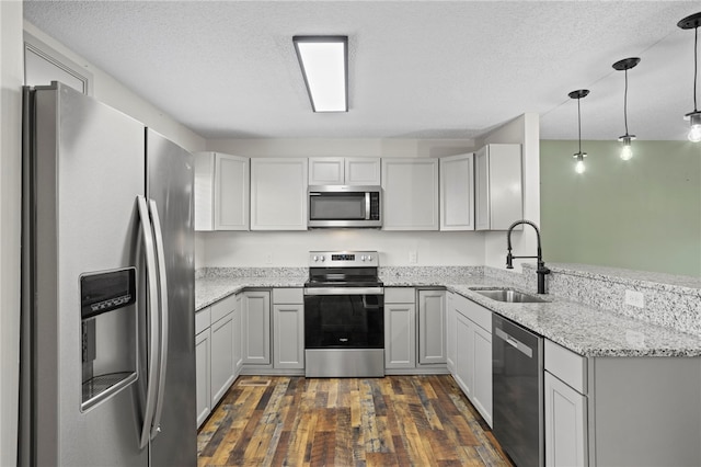 kitchen with pendant lighting, sink, dark hardwood / wood-style flooring, kitchen peninsula, and stainless steel appliances