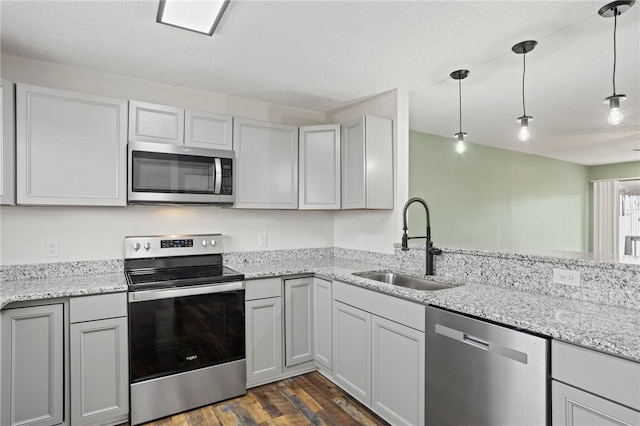 kitchen with appliances with stainless steel finishes, a textured ceiling, dark wood-type flooring, sink, and decorative light fixtures