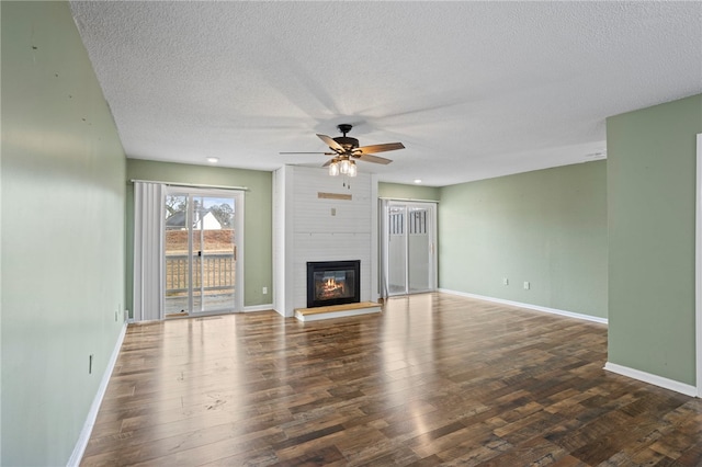 unfurnished living room featuring ceiling fan, a large fireplace, dark wood-type flooring, and a textured ceiling