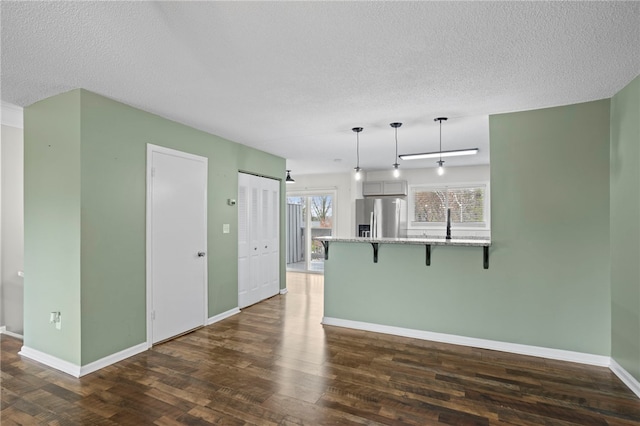 interior space with pendant lighting, dark wood-type flooring, stainless steel refrigerator with ice dispenser, a kitchen bar, and kitchen peninsula