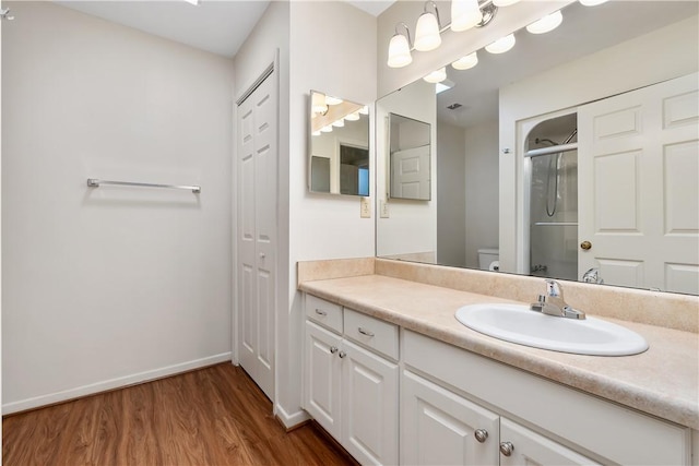 bathroom with a shower with shower door, toilet, wood-type flooring, and vanity