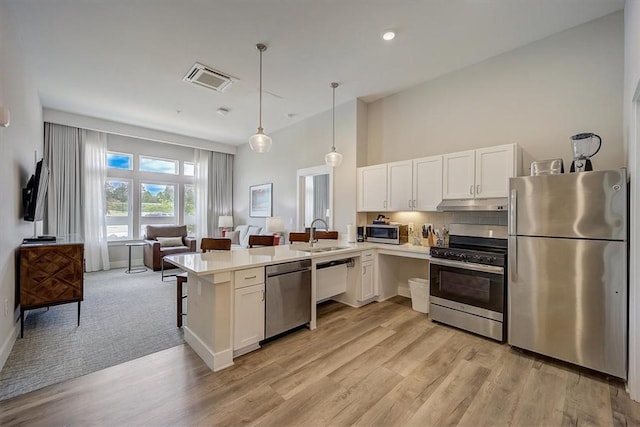 kitchen featuring pendant lighting, light wood-type flooring, appliances with stainless steel finishes, kitchen peninsula, and a breakfast bar area