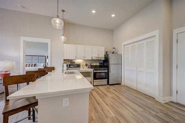 kitchen featuring a breakfast bar, white cabinets, decorative light fixtures, light hardwood / wood-style floors, and stainless steel appliances