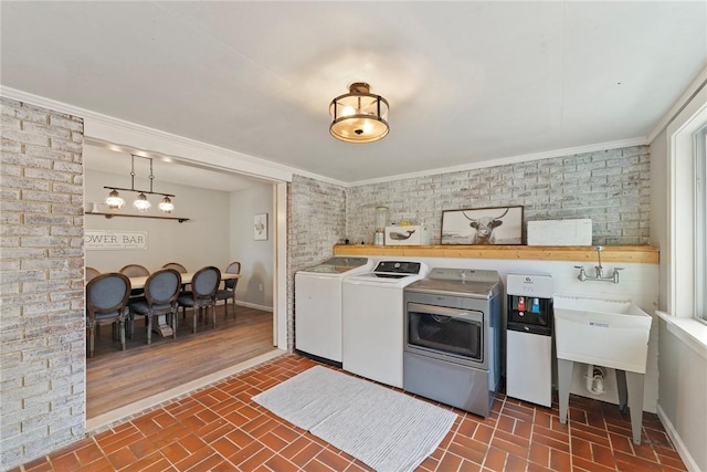 laundry room featuring washing machine and clothes dryer, brick wall, and ornamental molding