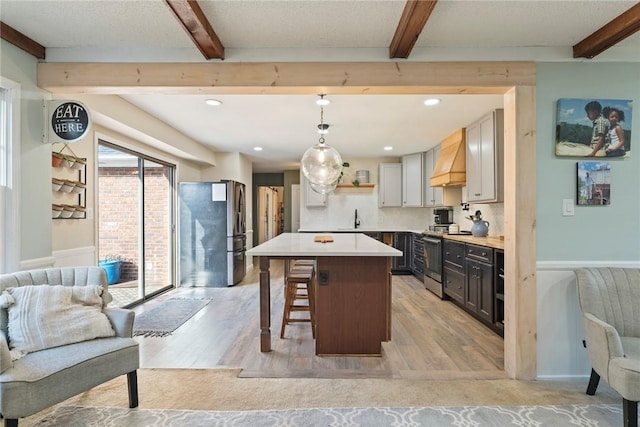 kitchen with appliances with stainless steel finishes, custom range hood, pendant lighting, beamed ceiling, and a center island