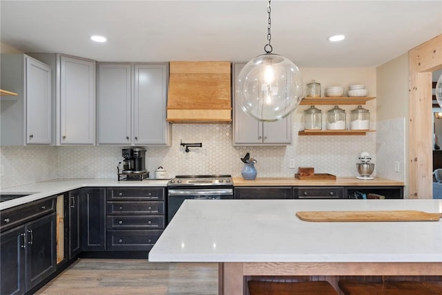 kitchen with backsplash, pendant lighting, stainless steel electric range, custom range hood, and hardwood / wood-style flooring