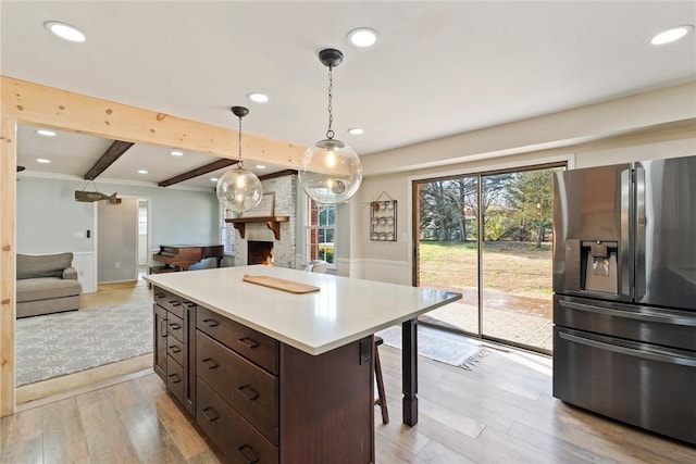 kitchen featuring stainless steel fridge, light wood-type flooring, a brick fireplace, beamed ceiling, and hanging light fixtures