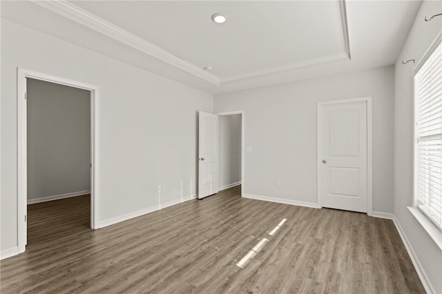 unfurnished bedroom featuring hardwood / wood-style flooring, a tray ceiling, and multiple windows