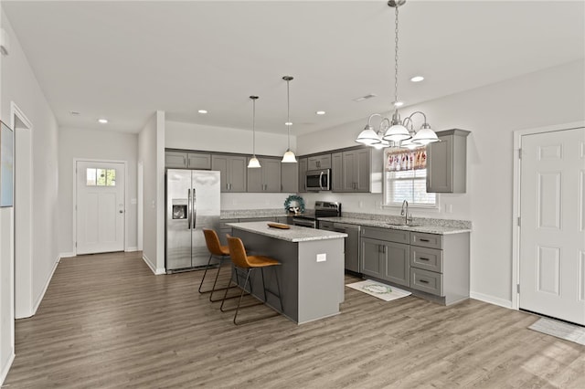 kitchen with sink, appliances with stainless steel finishes, pendant lighting, a kitchen island, and hardwood / wood-style flooring