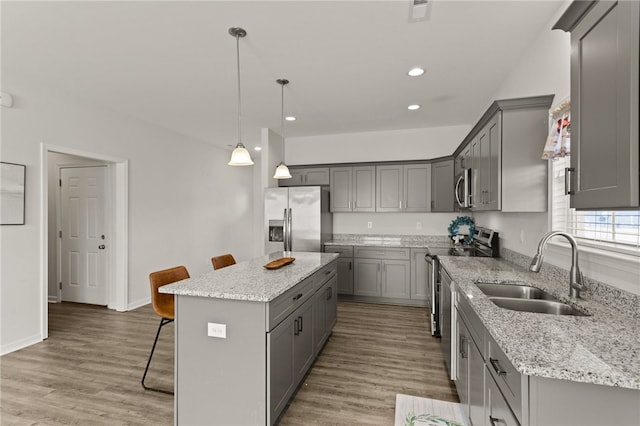 kitchen featuring a breakfast bar, a center island, sink, appliances with stainless steel finishes, and decorative light fixtures