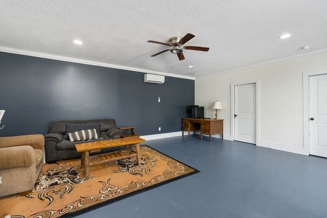 living room with ornamental molding, concrete flooring, a textured ceiling, a wall unit AC, and ceiling fan