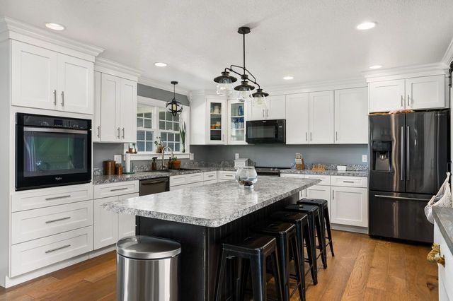 kitchen featuring black appliances, wood-type flooring, decorative light fixtures, white cabinets, and a kitchen island