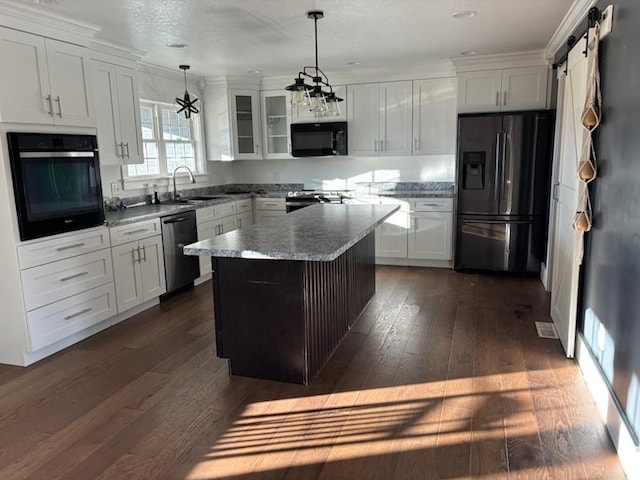 kitchen featuring black appliances, dark hardwood / wood-style floors, a barn door, decorative light fixtures, and a kitchen island