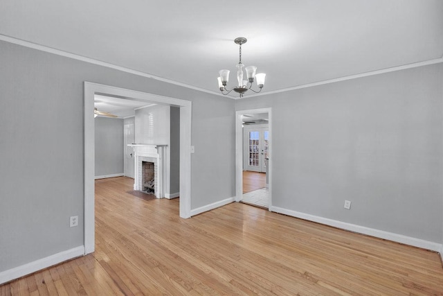 unfurnished dining area featuring a brick fireplace, ceiling fan with notable chandelier, crown molding, and light wood-type flooring