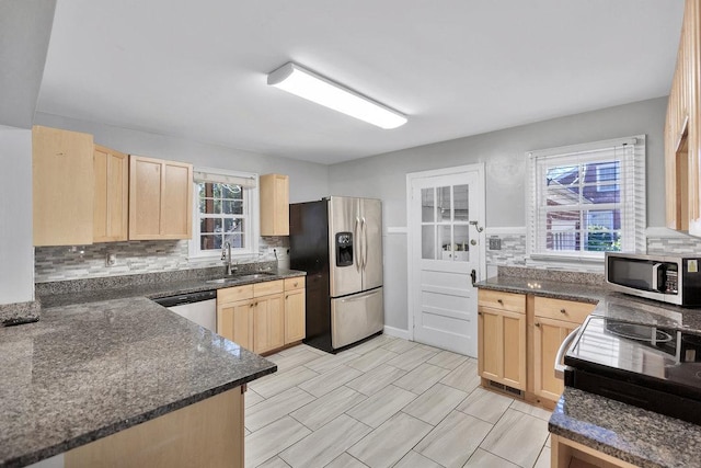 kitchen with stainless steel appliances, decorative backsplash, light brown cabinets, dark stone countertops, and sink