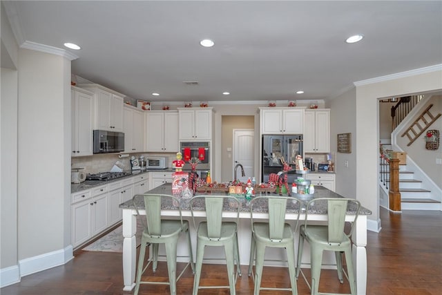 kitchen with white cabinets, dark hardwood / wood-style flooring, stainless steel appliances, and an island with sink